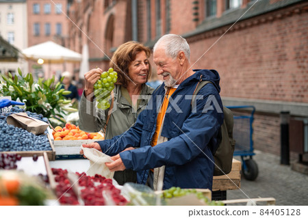 Happy senior couple tourists buying fruit outdoors on market in town. Happy senior couple tourists buying fruit outdoors on market in town. 84405128