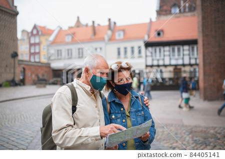 Senior couple tourists with face masks using map outdoors in town street Senior couple tourists with face masks using map outdoors in town street 84405141