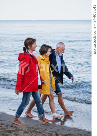 Side view of senior couple holding hands with their preteen granddaughter and walking on sandy beach Side view of senior couple holding hands with their preteen granddaughter and walking on sandy beach 84405142