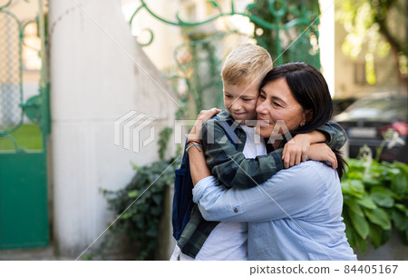 Happy schoolboy hugging his grandmother waiting for him after school outdoors in street. Happy schoolboy hugging his grandmother waiting for him after school outdoors in street. 84405167