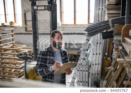 Mature male carpenter doing inventory indoors in carpentry workshop. Small business concept. 84405767