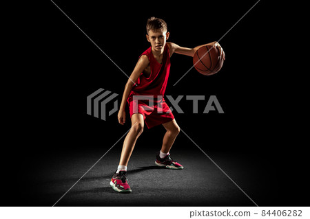 Full-length portrait of teen boy, professional backetball player in motion, training isolated over black background. Dribbling action 84406282