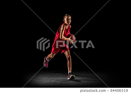 Full-length portrait of teen boy, basketball player in motion, training, running with ball isolated over black background. Goal scoring 84406319