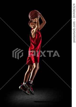 Full-length portrait of teen boy, basketball player training, throwing ball into the basket in a jump isolated over black background 84406324