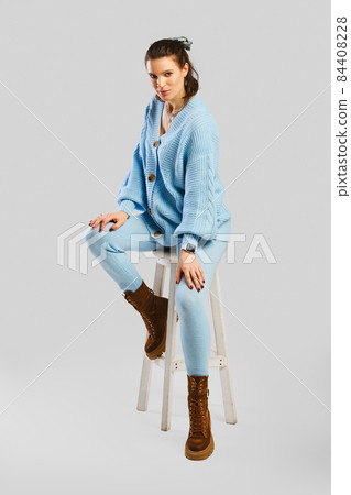 Full length portrait of beautiful woman in light blue warm knitted tracksuit sitting on stool Full length portrait of beautiful woman in light blue warm knitted tracksuit sitting on stool 84408228