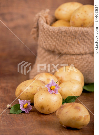 Raw potatoes with flowers in the bag on the wooden background Raw potatoes with flowers in the bag on the wooden background 84408634