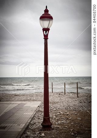 Red vintage street light by the sea in a cloudy day. Red vintage street light by the sea in a cloudy day. 84408700