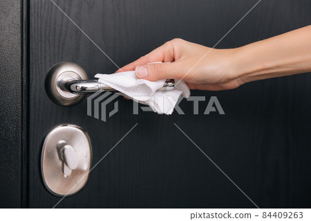 Cleaning black door handles with an antiseptic wet wipe. Sanitize surfaces prevention in hospital and public spaces against corona virus. Woman hand using towel for cleaning home room door link. Cleaning black door handles with an antiseptic wet wipe. Sanitize surfaces prevention in hospital and public spaces against corona virus. Woman hand using towel for cleaning home room door link. 84409263