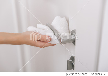 Cleaning black door handles with an antiseptic wet wipe. Sanitize surfaces prevention in hospital and public spaces against corona virus. Woman hand using towel for cleaning. 84409307