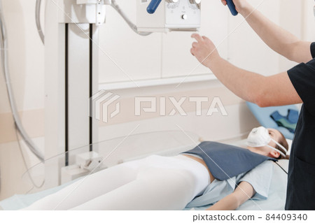Doctor taking x-ray of patient lying on gurney. Hospital radiology room. Technician adjusting an x-ray machine. Female lying on a bed is scanning chest, heart, lungs in modern clinic office. 84409340