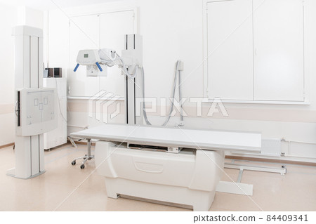 X-ray department in modern hospital. Radiology room with scan machine with empty bed. Technician adjusting an x-ray machine. Scanning chest, heart, lungs in modern clinic office. 84409341