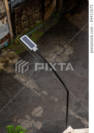 Rain falls on a small solar panel behind a street lamp in a small alley Rain falls on a small solar panel behind a street lamp in a small alley 84411675