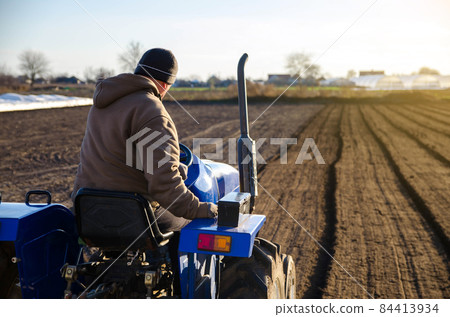 The tractor is cultivating the soil in the farm field. Farming. Agriculture agribusiness. preparing for cutting rows for the next sowing season in the spring. Softening and improving soil qualities. The tractor is cultivating the soil in the farm field. Farming. Agriculture agribusiness. preparing for cutting rows for the next sowing season in the spring. Softening and improving soil qualities. 84413934