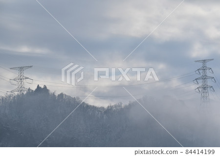 Two power transmission towers standing on top of a cloudy mountain Two power transmission towers standing on top of a cloudy mountain 84414199