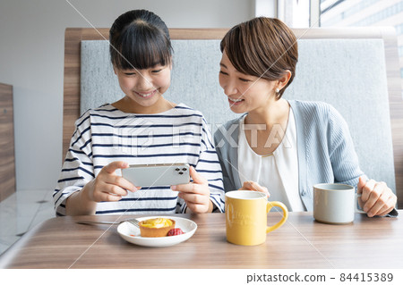 Junior high school student and mother taking pictures of dessert with a smartphone at a family restaurant 84415389