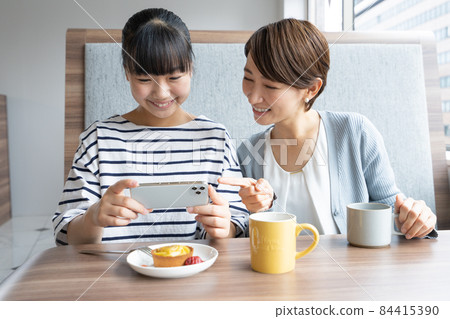 Junior high school students and moms taking pictures of desserts on their smartphones at a family restaurant 84415390