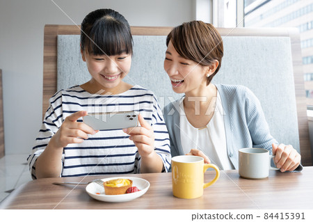 Junior high school students and mothers taking pictures of desserts on their smartphones at a family restaurant 84415391