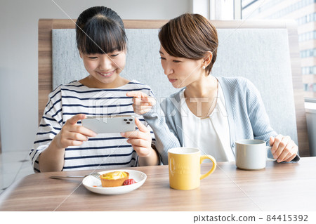 Junior high school students and mothers taking pictures of desserts on their smartphones at a family restaurant 84415392