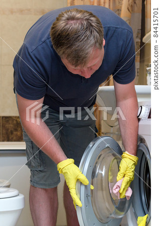 An adult man is cleaning the bathroom, wiping the dust from the washing machine An adult man is cleaning the bathroom, wiping the dust from the washing machine 84415701