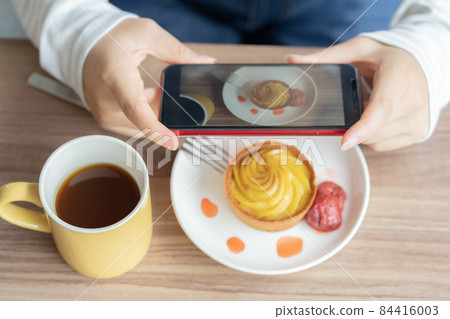 Up the hand of a girl who takes a picture of a tart with a smartphone Up the hand of a girl who takes a picture of a tart with a smartphone 84416003