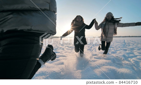 Cheerful girls run across the snow-covered field. 84416710