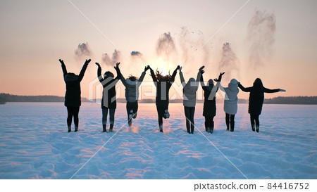 A group of girls friends are throwing snow up at sunset. 84416752