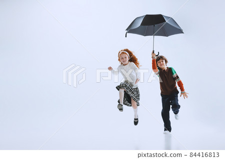 Two happy kids, boy and girl running with umbrella isolated on white studio background. Childhood, dreams, imagination, education 84416813