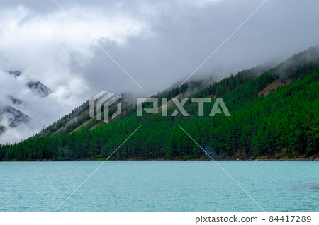 Shavlinskoye lake in the Altai Republic on the background of mountain peaks shrouded in fog. Shavlinskoye lake in the Altai Republic on the background of mountain peaks shrouded in fog. 84417289