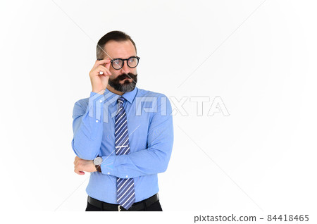 Portrait of confident middle-aged businessman in blue shirt and wearing glasses with a beard and mustache standing on white background with copy space Portrait of confident middle-aged businessman in blue shirt and wearing glasses with a beard and mustache standing on white background with copy space 84418465