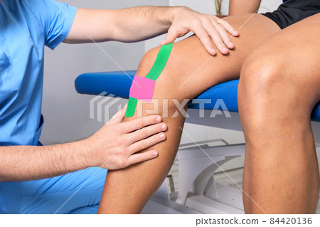 Physical therapist applying kinesio tape on male patient knee. Kinesiology, physical therapy 84420136
