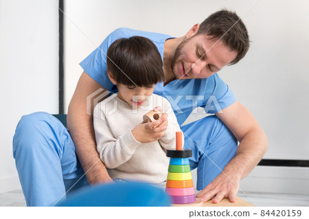 Young therapist helping cute little boy who has cerebral palsy, playing with developing toy at Young therapist helping cute little boy who has cerebral palsy, playing with developing toy at 84420159