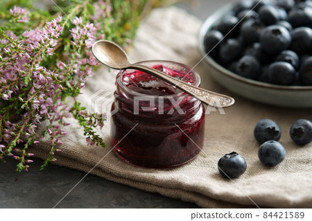 Small jar of blueberry jam and plate of fresh ripe blueberries on kitchen table. 84421589