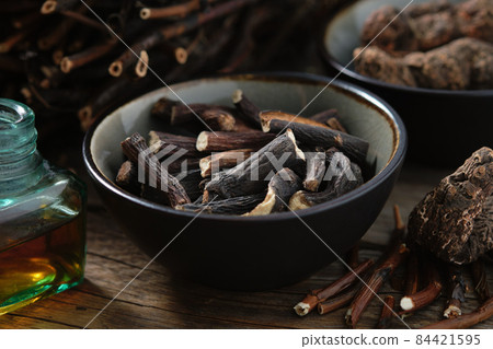 Black bowl of Common comfrey or symphytum officinale roots. Bottle of infusion or tincture. Dried comfrey officinalis roots, knitbone and Bistort, Snakeweed, Snake roots. Alternative herbal medicine. Black bowl of Common comfrey or symphytum officinale roots. Bottle of infusion or tincture. Dried comfrey officinalis roots, knitbone and Bistort, Snakeweed, Snake roots. Alternative herbal medicine. 84421595