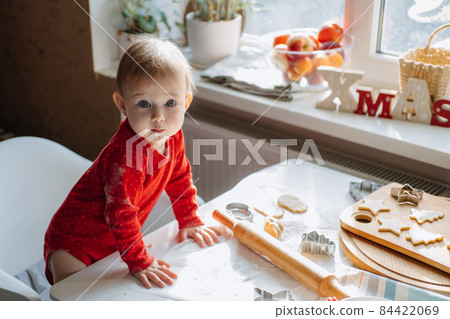 Cute little baby toddler girl making christmas cookies in home kitchen and play with dough. Mother and little girl baking Christmas gingerbread pastry for family dinner on Xmas eve. 84422069