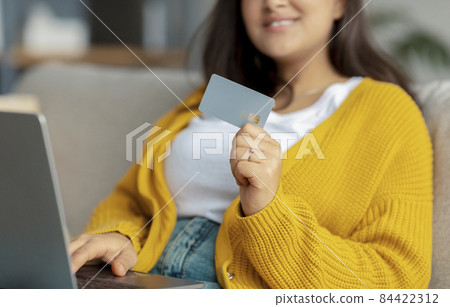 Online shopping. Cropped view of arab woman with laptop and credit card making purchases remotely from home, closeup Online shopping. Cropped view of arab woman with laptop and credit card making purchases remotely from home, closeup 84422312