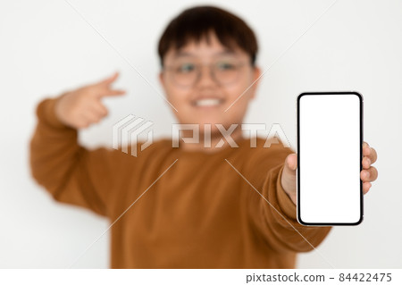 Cute korean teenager pointing at cellphone with empty screen, mockup 84422475