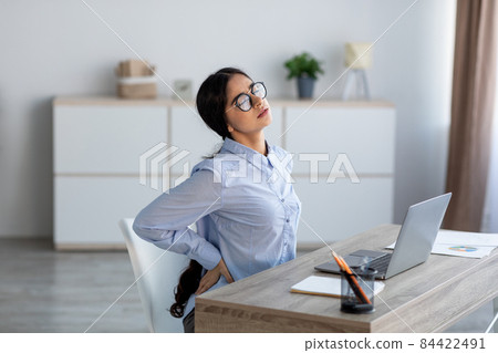 Tired upset young indian business woman suffering from back pain, muscle spasm at workplace with laptop 84422491