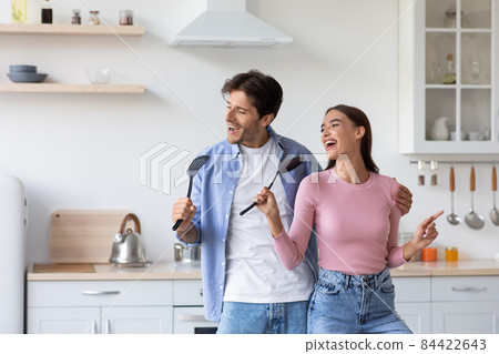 Cheerful young caucasian couple sing in imaginary microphone, have fun and dance in modern kitchen 84422643
