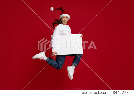 Crazy Offer. Cheerful Woman In Santa Hat Jumping With Blank White Placard Crazy Offer. Cheerful Woman In Santa Hat Jumping With Blank White Placard 84422784