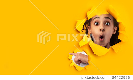 Shocked african american teenage girl with open mouth looks through hole on yellow paper 84422936