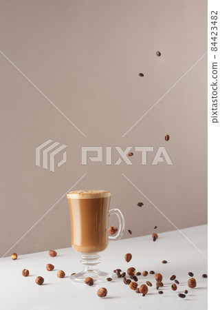 Glass cup with cappuccino and fragrant foam, coconut milk, hazelnuts, planted coffee beans. Coffee concept with vegetarian milk. Cup with cappuccino, latte or coffee with milk. Glass cup with cappuccino and fragrant foam, coconut milk, hazelnuts, planted coffee beans. Coffee concept with vegetarian milk. Cup with cappuccino, latte or coffee with milk. 84423482