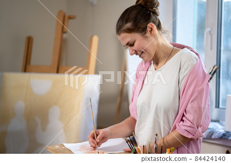 Female artist working in studio. Creative workspace, painting class, easel with canvas, art therapy. Inspiration, creativity, talent, craft concept. Artist studio interior. People, leisure and hobby 84424140