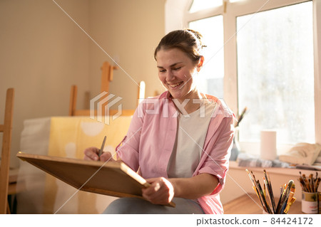 Cute woman paints on canvas in an art workshop. Artist creating picture. Art school or studio. Work with paints, brushes and easel. Hobby and leisure concept. Woman painter at workspace 84424172