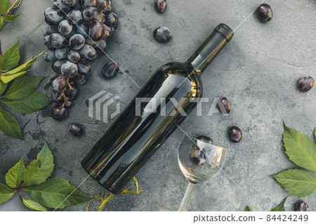 Bottle of red wine, green vine, wineglass and ripe grape on vintage dark stone table background. Top view copy space for text. Wine shop wine bar winery or wine tasting concept Bottle of red wine, green vine, wineglass and ripe grape on vintage dark stone table background. Top view copy space for text. Wine shop wine bar winery or wine tasting concept 84424249