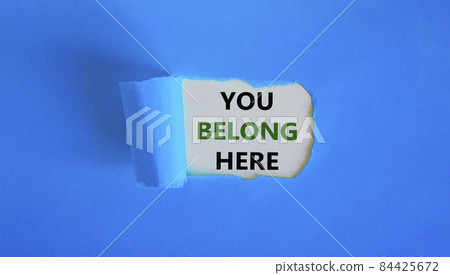 You belong here symbol. Concept words 'You belong here' appearing behind torn blue paper. Beautiful background. Business and you belong here, better inclusion concept. Copy space. 84425672
