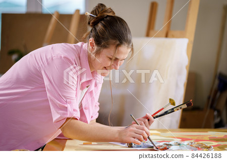Cute woman paints on canvas in an art workshop. Artist creating picture. Art school or studio. Work with paints, brushes and easel. Hobby and leisure concept. Woman painter at workspace 84426188