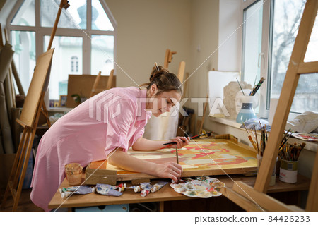 Cute woman paints on canvas in an art workshop. Artist creating picture. Art school or studio. Work with paints, brushes and easel. Hobby and leisure concept. Woman painter at workspace 84426233