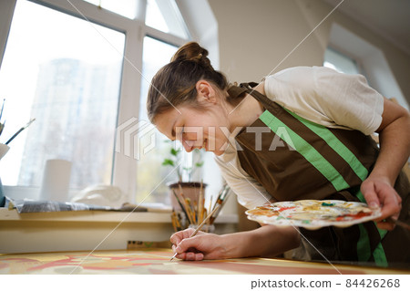 Cute woman paints on canvas in an art workshop. Artist creating picture. Art school or studio. Work with paints, brushes and easel. Hobby and leisure concept. Woman painter at workspace 84426268