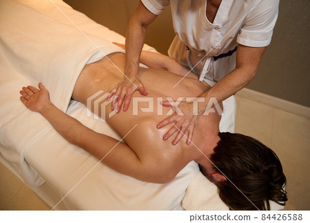 Top view of unrecognizable professional masseuse giving medical therapy massage to young man's back muscles relaxing on massage table at health spa center. Ayurvedic and alternative therapy concept 84426588