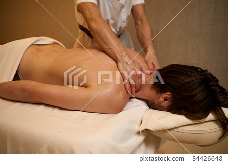 Focus on the hands in massage oil of unrecognizable physiotherapist massaging the man's back and shoulders in wellness spa clinic. Spa center male client getting therapeutic Ayurvedic body treatment Focus on the hands in massage oil of unrecognizable physiotherapist massaging the man's back and shoulders in wellness spa clinic. Spa center male client getting therapeutic Ayurvedic body treatment 84426648